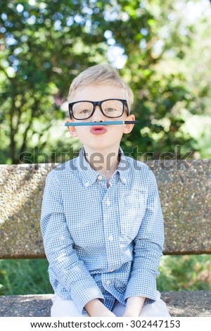 funny schoolboy playing with pencil and being silly ready for school enjoying warm weather in the park