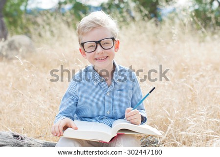 smiling schoolboy in glasses studying ready for school enjoying warm weather in the park