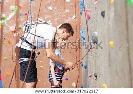 young father preparing his little son for climbing in indoor gym