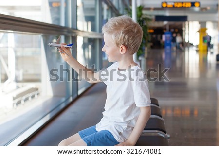 smiling caucasian boy playing with toy plane in the airport waiting for travel departure
