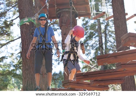 positive little boy and his father climbing at outdoor treetop adventure park being active and healthy together