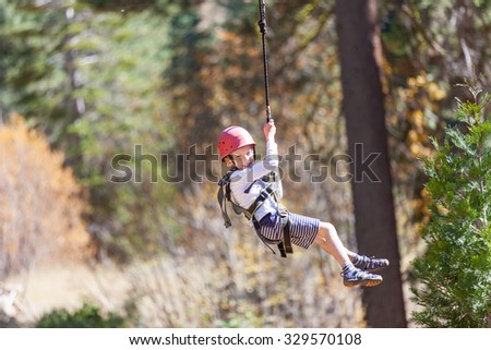 positive little boy ziplining at outdoor treetop adventure park being active and brave