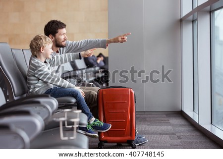 positive smiling boy and his father waiting at the airport for plane departure and pointing with fingers at something, vacation and travel concept