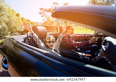 excited family of two, young father and his smiling son with hands high up in the air, enjoying road trip in convertible car, journey and vacation concept, sun flare