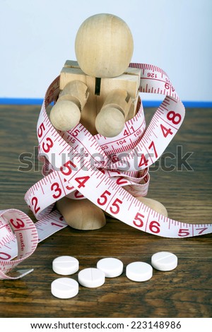 Weight loss concept with wooden man wrapped in measuring tape and diet pills