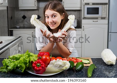 Woman making food in kitchen preparing salad holding lettuce head while smiling happy.