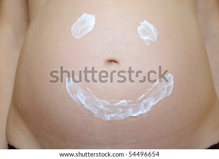Smiling face painted on pregnant belly with moisturizer cream