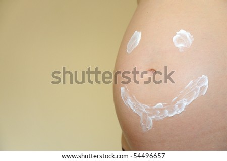 Smiling face painted on pregnant belly with moisturizer cream
