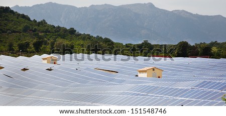 Field of solar panels at photovoltaic power plant with two service buildings.