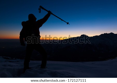 At sunset a man stands on a snowy peak expressing his joy for have reached the top of a mountain peak. Concept: adventure, achievement, sport.