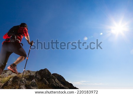 Skyrunner runs uphill along a mountain trail. Rear view, caucasian young man. Sunny summer day. West Alps, Europe.