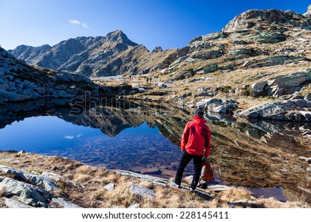 Male hiker standing in front of a mountain lake. Autumn sunny day, italian Alps, Europe..