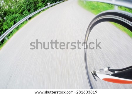 Road bike; detail of the front wheel while the bike goes downhill at high speed, large copy space of the left side. Sport and active life concept. Intentional motion blur effect.
