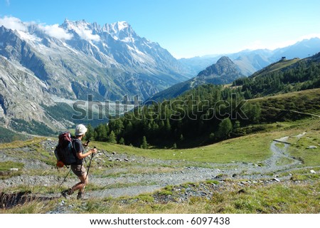Trekker walking along a mountain path, in background the Mont Blanc valley, west Alps, Italy.