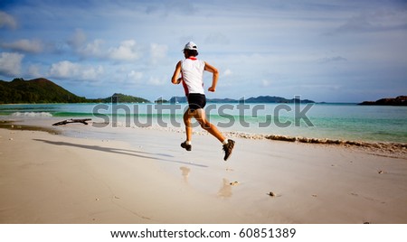One young man running on a tropical empty beach at sunrise; Seychelles, Indian ocean