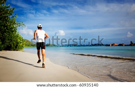 One young man running on a tropical empty beach at sunrise, rear view ; Seychelles, Indian ocean