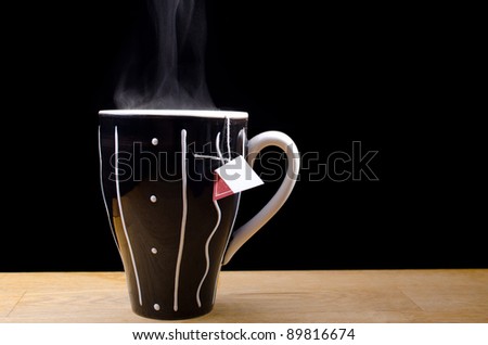 Steaming hot cup of tea on a table with black background