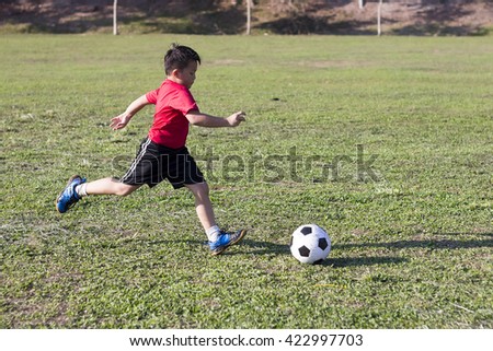 young boy kick soccer ball in green grass field, kid athlete with jersey training football in sunny outdoor park
