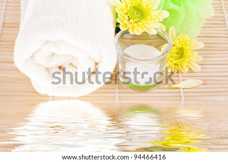 Towel, flowers, candle and bamboo mat near water reflection. Spa concept