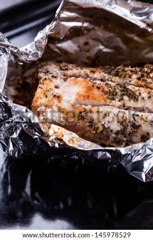 baked pork meat with seasoning in foil on black tray