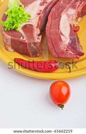 The vertical frame on which a plate with two slices of fresh meat and fiery red pepper pod. Nearby is a small tomato. All on a light background.
