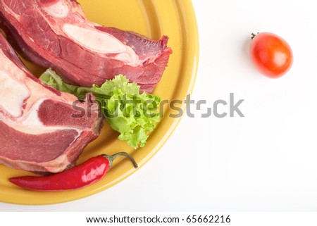 Pieces of raw meat on a plate with a pod of red hot pepper and tomato for cooking the main hot meal on the grill.