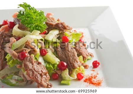 Salad from slices of the fried beef, cucumbers and a cowberry with sauce from olive oil of balsam vinegar on a light plate. A shot horizontal, focus in the center a shot