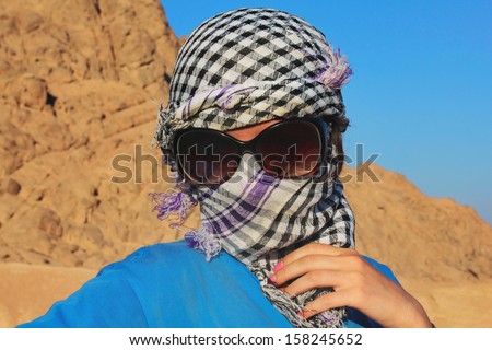 Portrait of a young girl in a scarf, sunglasses in the desert on a background of mountains and blue sky
