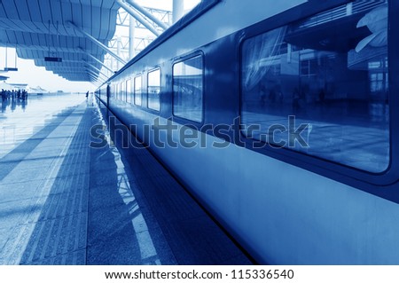 Covered railway station with trains and silhouettes of hurrying people