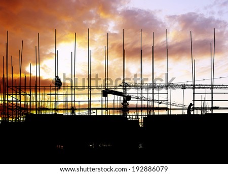 Construction site, silhouettes of construction industry workers on scaffolding against the sunset light.