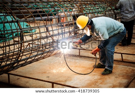 welder worker welding metal by electrode with bright electric arc and sparks during manufacture of metal equipment