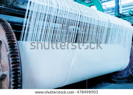 A row of textile looms weaving cotton yarn in a textile mill.