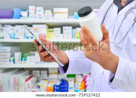 Pharmacist holding medicine bottle and computer tablet for filling prescription in pharmacy drugstore.