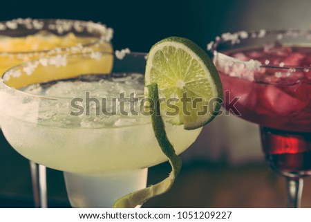 Lime margarita, orange margarita and cherry margarita cocktail mix in salt rimmed glasses garnished with slices of lime, orange and cherries. Selective focus on the lime slice