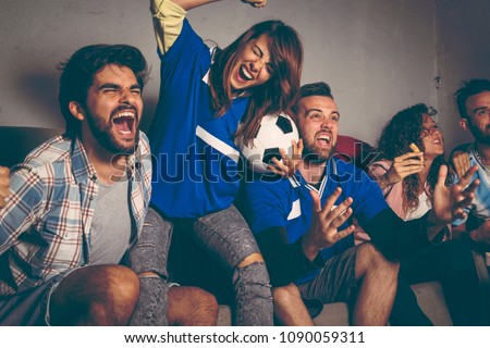 Group of young friends watching a football match on a building rooftop, celebrating after their team has scored a goal. Focus on the man in the middle.