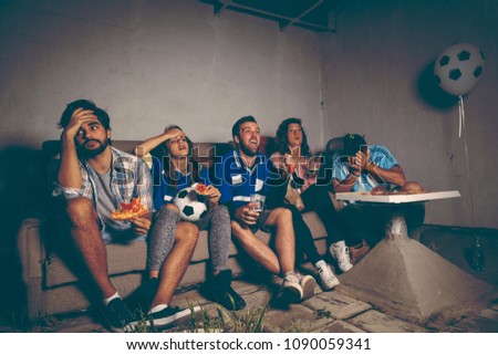Group of young friends watching a football match on a building rooftop, cheering eating pizza and drinking beer, disappointed after they lost the match