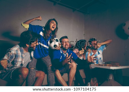 Group of young friends watching a football match on a building rooftop, celebrating after their team has scored a goal
