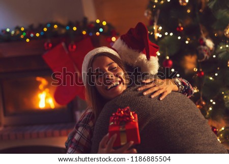 Young couple in love sitting by the fireplace and nicely decorated Christmas tree, exchanging Christmas presents