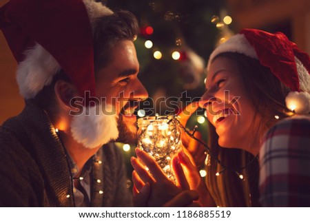 Young couple in love sitting by the fireplace and nicely decorated Christmas tree, enjoying the Christmas magic. Focus on the man