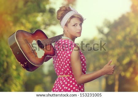 Young woman hitchhiking along the road with guitar in hand
