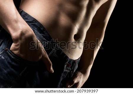 Athletic built young man with well-defined abdominal and pectoral muscles isolated on a black background