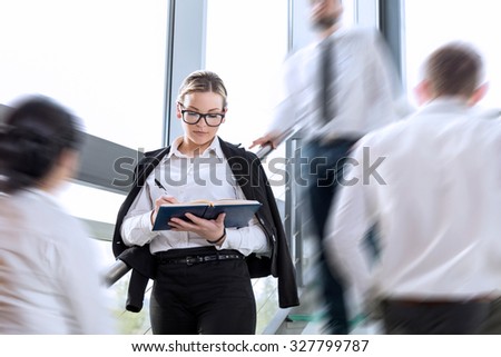 Busy office building corridor, three business people in a motion, focus on woman standing and taking notes