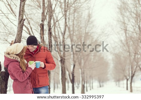 Young couple in love on a winter vacation, standing next to a tree, chatting and drinking hot cup of tea