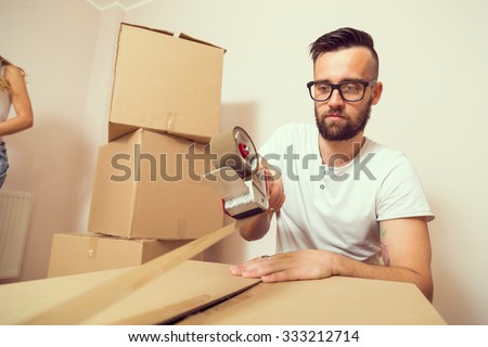 Young man packing things and taping boxes, preparing for moving out the apartment