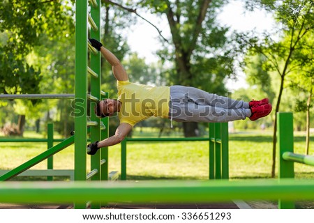 Young athlete working out in an outdoor gym, doing street workout exercises