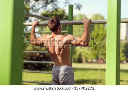 Muscular built young athlete working out in an outdoor gym, doing chin-ups
