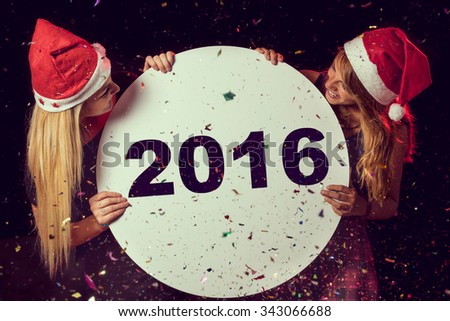 Two beautiful young girls enjoying at New Year\'s Eve party, holding cardboard circle with 2016 written on it