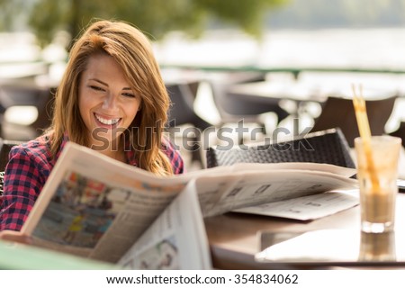 Beautiful young brunette sitting in a cafe, drinking coffee and reading newspapers
