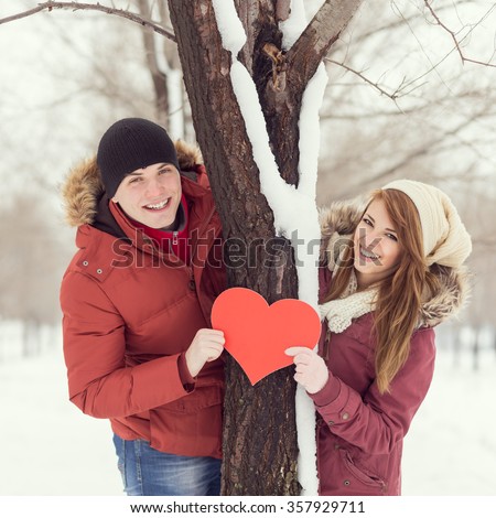 Couple in love looking at the camera, holding red heart, standing next to a three