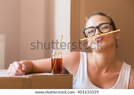 Young girl moving in a new apartment, sitting on the floor, drinking ice tea, surrounded with cardboard boxes